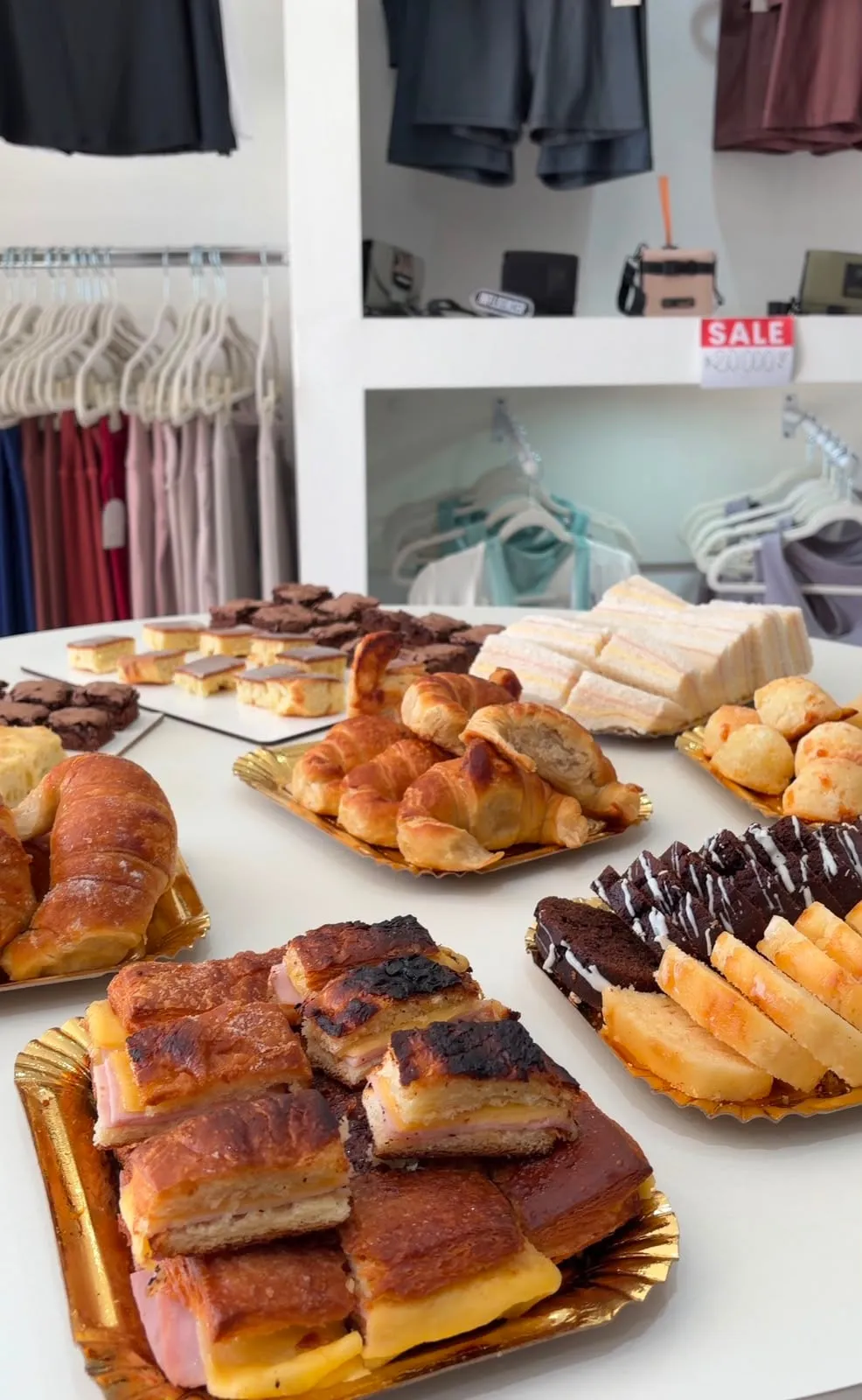 Mesa dulce servida con medialunas, sándwiches de miga, brownies y alfajores en bandejas